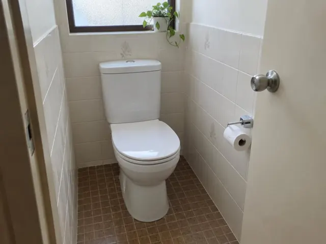 Clean white toilet in a tiled bathroom with a window and brown floor tiles in Eastgardens